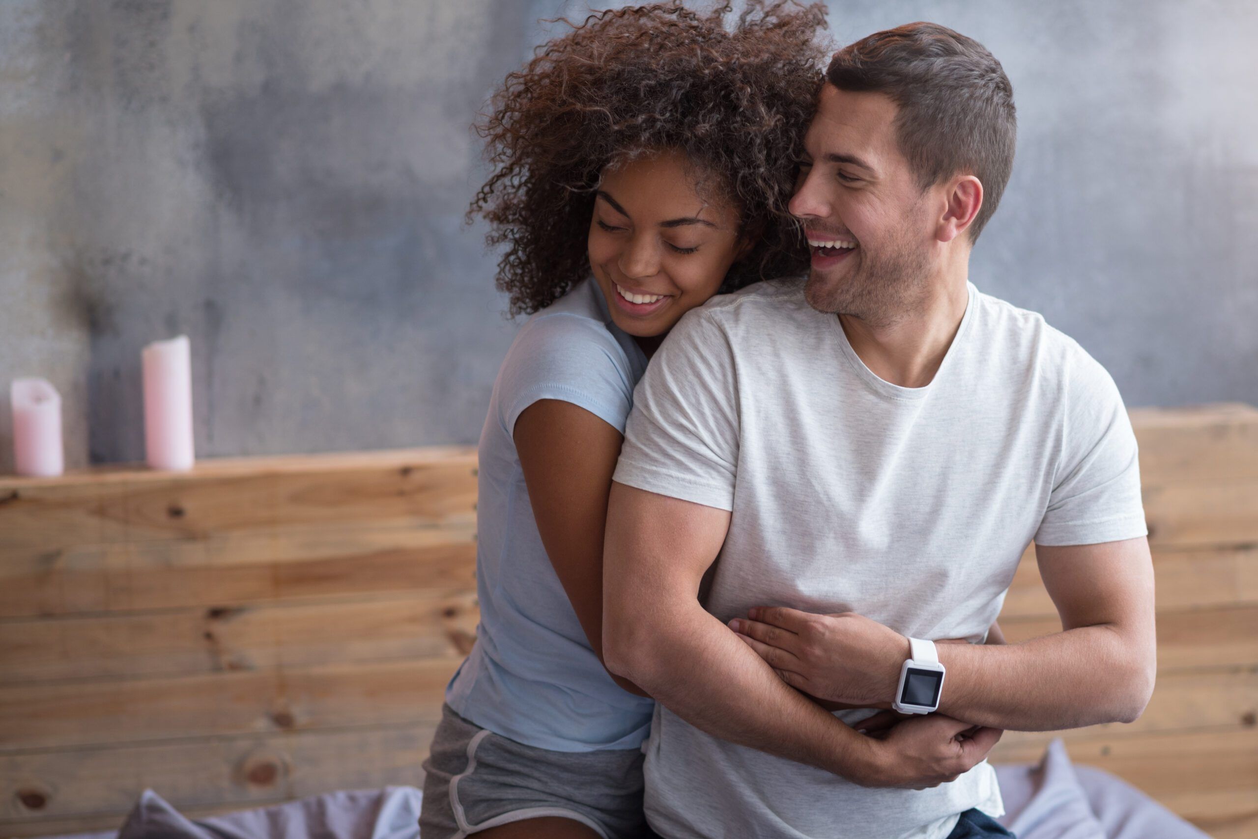 Stay here. Happy sweet young couple smiling while embracing each other spending honeymoon morning together in bed.