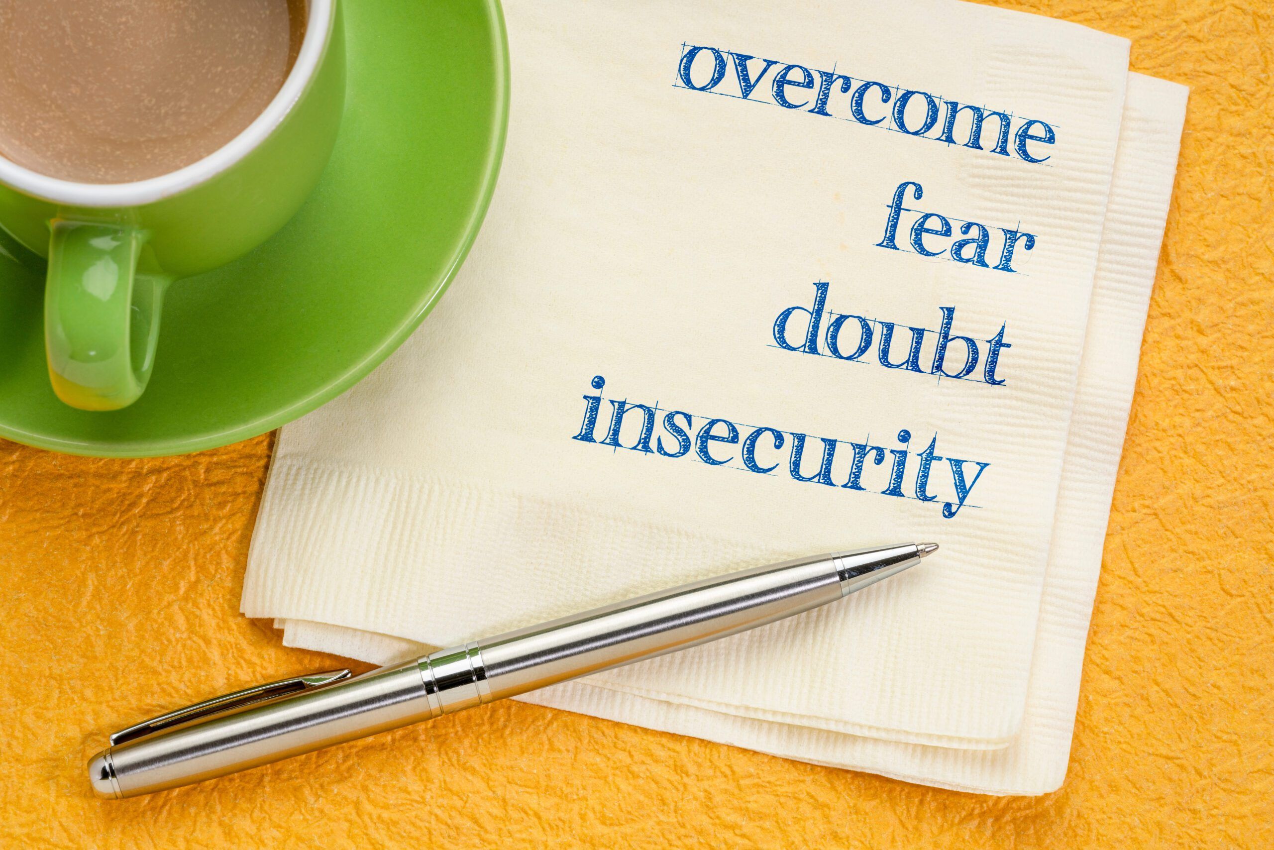 overcome fear, doubt, insecurity - handwriting on a napkin with a cup of coffee