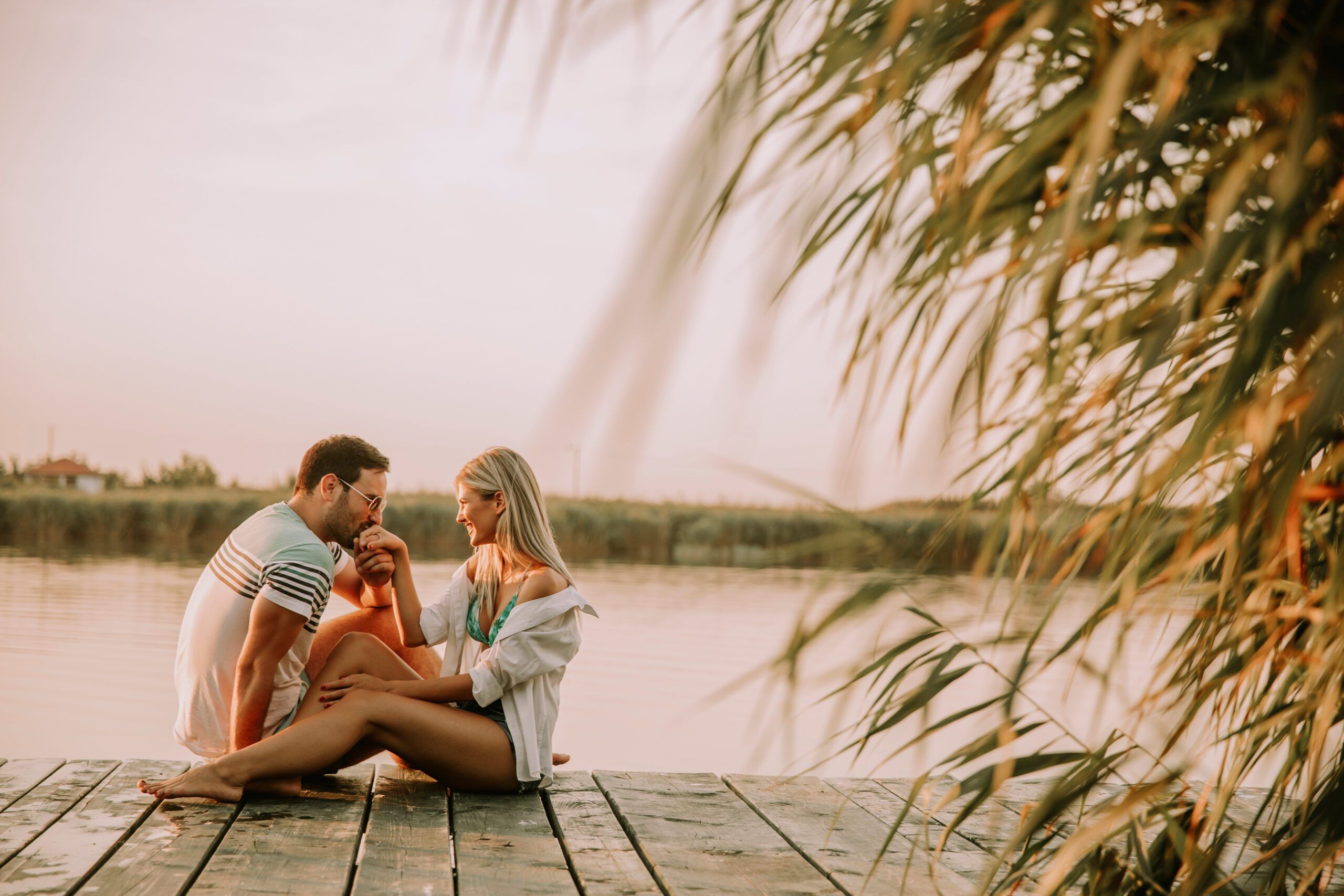 Romantic couple sitting on the wooden pier on the lake at sunny day