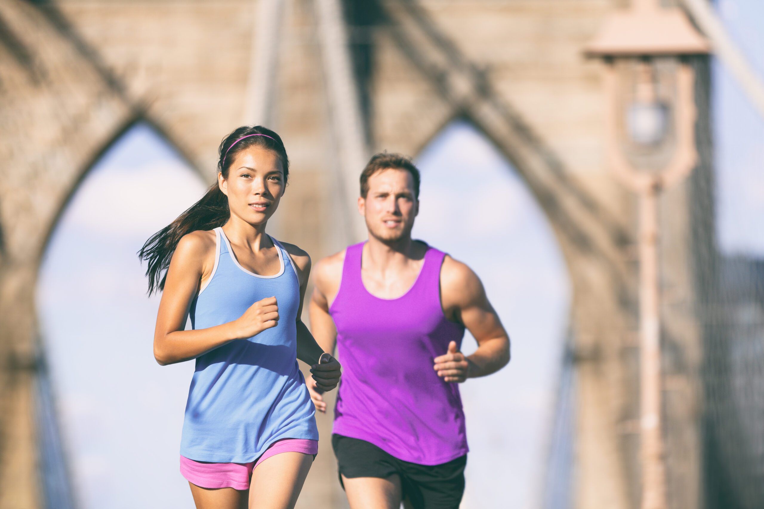 New York city runners running training for marathon on Brooklyn bridge NYC in urban cityscape. Fit young couple doing their workout routine on a summer day.